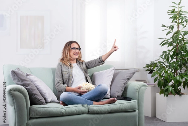 Fototapeta Young woman with smart glasses touching interface while holding popcorn