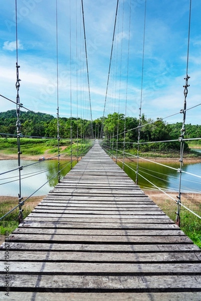 Obraz Wooden footbridge in nature tropical forest for trail route. Walking swing bridge, a suspension bridge across jungle, path way at Kaeng Krachan National Park, Phetchaburi Province,Thailand. Vertical.