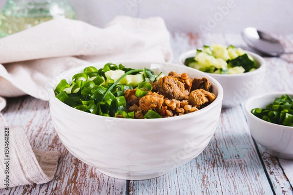Fototapeta Buckwheat porridge with meat, cucumber and chives in a bowl on the table