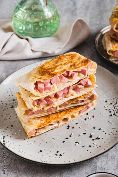 Fototapeta Crispy envelopes with sausage and cheese in flat bread on a plate on the table vertical view