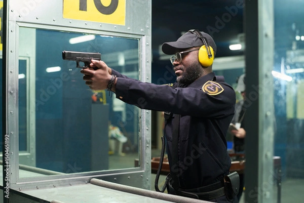 Fototapeta African American officer practicing marksmanship wearing earmuffs and safety equipment at shooting range aiming firearm reflecting focus and precision