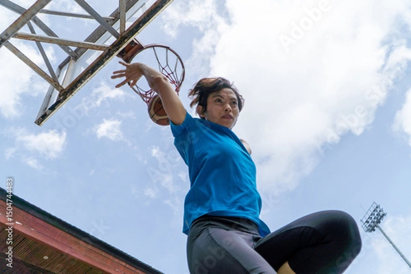 Fototapeta Denpasar, 13 Feb 23: A young athlete performs a slam dunk at a street basketball court under the midday sun in Bali, Indonesia.