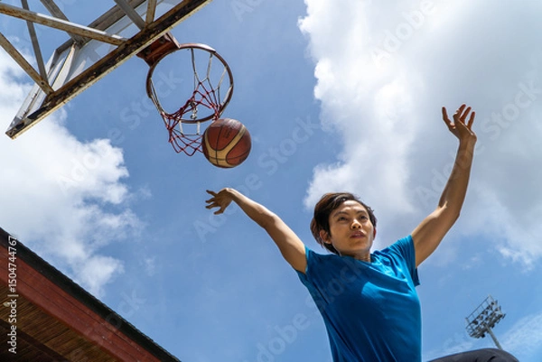 Fototapeta Denpasar, 13 Feb 23: A young athlete performs a slam dunk at a street basketball court under the midday sun in Bali, Indonesia.