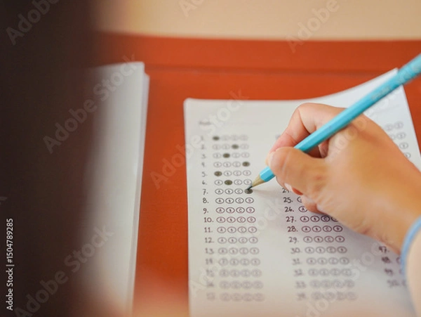 Fototapeta Closeup of female student's hand doing exam in classroom. School proficiency test. Asian student doing exam. Education, learning