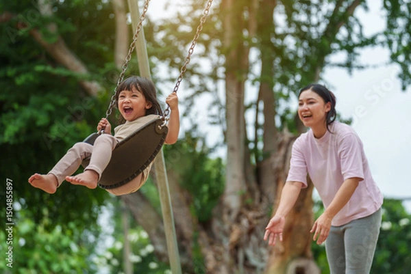Fototapeta cheerful toddler girl with mother playing on a swing at playground