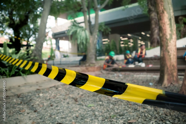Fototapeta Striped black and yellow safety line stretched out around building renovation area with construction workers on the background