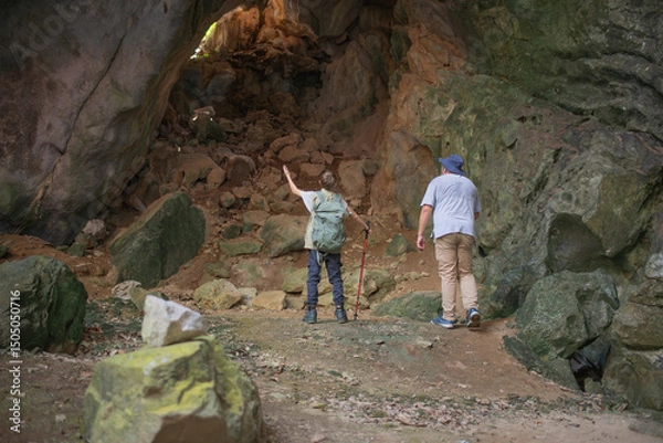 Fototapeta Tourist trekking with backpack and using a walking stick, gesturing forward suggesting of adventure or discovery in cave mysterious and ancient outdoor adventure concept.