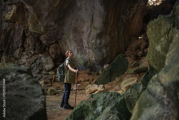 Fototapeta Tourist trekking with backpack and using a walking stick, gesturing forward suggesting of adventure or discovery in cave mysterious and ancient outdoor adventure concept.