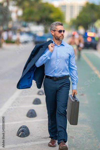 Fototapeta Businessman walk to work. Hispanic businessman walking on the street confidently. Office worker on way to office. Middle-aged businessman walking on city. Businessman in a summer outfit walking.