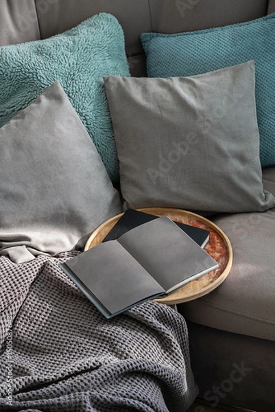 Fototapeta Cozy Living Room Scene Featuring a Gray Sofa with Decorative Pillows, Soft Blanket and an Open Book on Wooden Tray.
