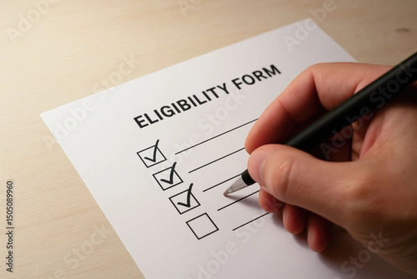 Fototapeta A person is checking boxes on an eligibility form with a pen on a light wooden surface.