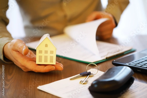 Obraz Businessman Holding Miniature House, Reviewing Real Estate Documents and Contracts with House Keys on Desk