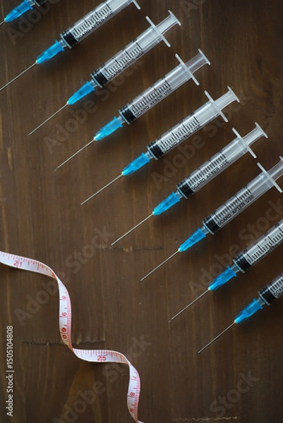 Obraz Medical Syringes with Measurement Tape on Wooden Surface - Health Care and Vaccination Concept