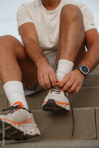 Fototapeta Close-up of a sportsman tying shoelaces on his running shoes, preparing for training session outdoors