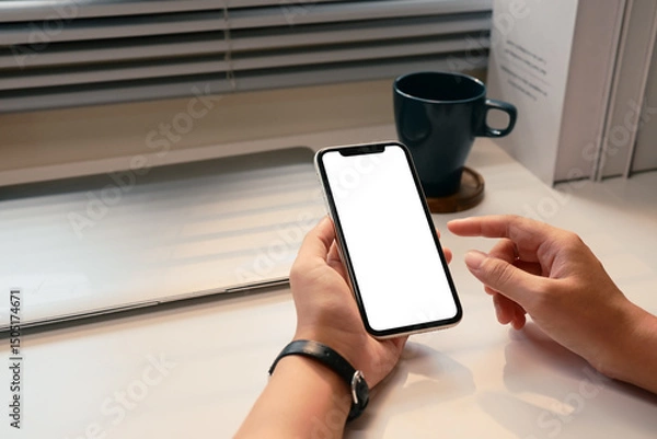 Fototapeta Close up of hands holding smartphone with blank screen at desk with natural light