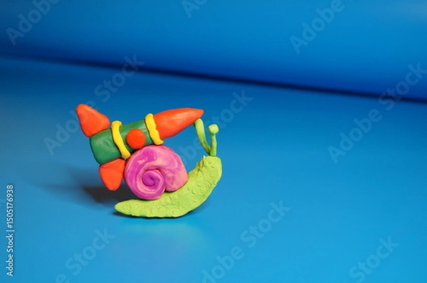 Fototapeta A toy snail made of plasticine with a rocket on a blue background.