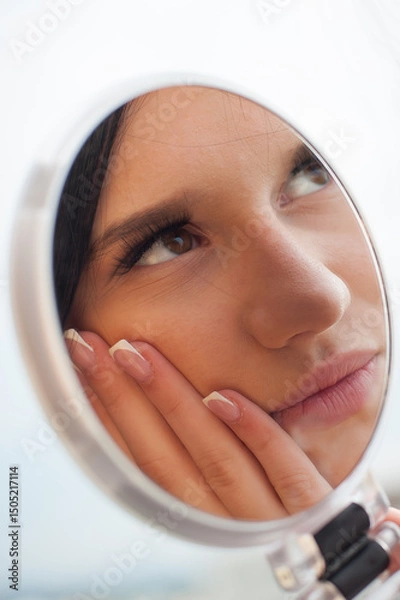 Obraz A young woman holds a round mirror, looking at her reflection. She is touching her cheek and posing for social media, showcasing a fashionable and modern aesthetic