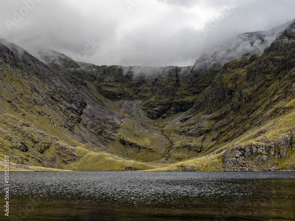 Fototapeta Misty mountain lake nestled in a rugged valley, a serene yet dramatic scene of nature's power and quiet beauty.