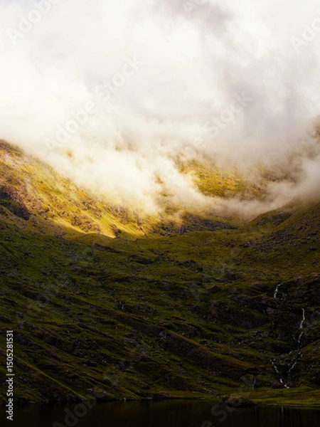 Fototapeta A grassy hillside slopes down towards the dark waters of Lough Callee. Clouds hang in the sky at the top of the hill, creating a calm and exciting landscape in Ireland.