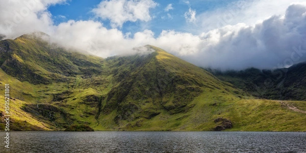 Fototapeta Lough Callee showcases stunning emerald hills enveloped in clouds, creating a serene natural vista. The calm waters mirror the landscape, highlighting Ireland's scenic charm.