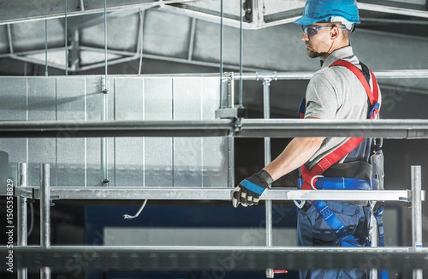Fototapeta Worker in Safety Gear Installs HVAC System in Industrial Building During Daytime Projects