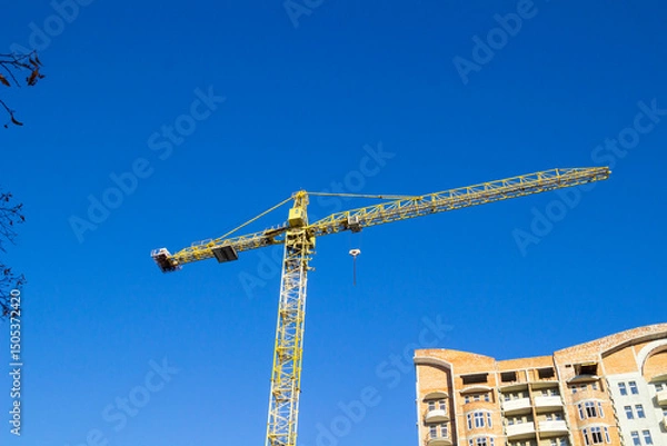 Fototapeta A construction crane and a part of an unfinished house made of ceramic bricks against ablue sky.
