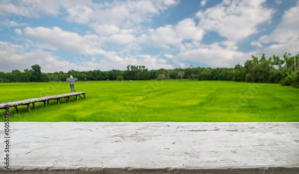Fototapeta empty cement old table on blur rice field and cloud background, for your product placement or montage with focus to the table top in the foreground. blank shelf, shelves with copy space