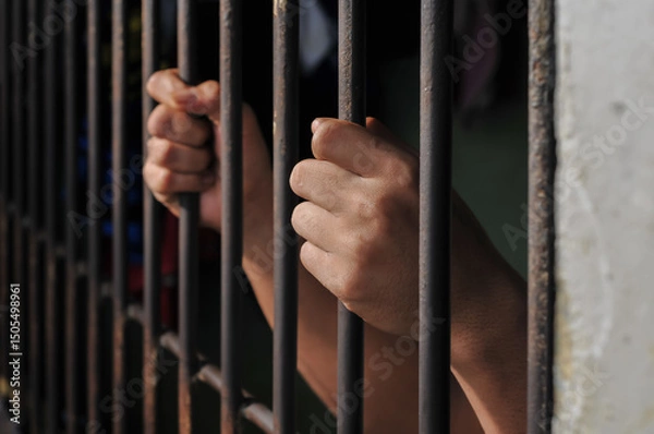 Obraz Hands of a prisoner behind prison bars on black background