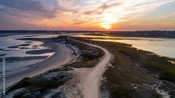 Obraz Winding Dirt Road Through Coastal Marshland Towards Distant Buildings at Golden Sunset with Reflective Tidal Pools
