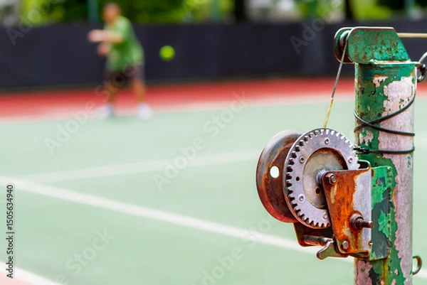 Fototapeta Old and rustic tennis net reel post with blurred person taking tennis lesson on the background