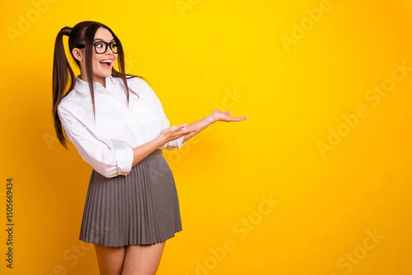 Fototapeta Young woman with ponytails wearing stylish attire gestures energetically against a yellow background, expressing cheerful vibrance