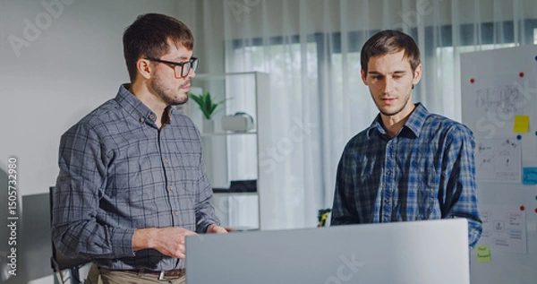 Fototapeta Team adult male engineer collaborate on robotic hand project using AI code solutions machine learning at tech workspace. Artificial intelligence interface, collaboration support prototype development.
