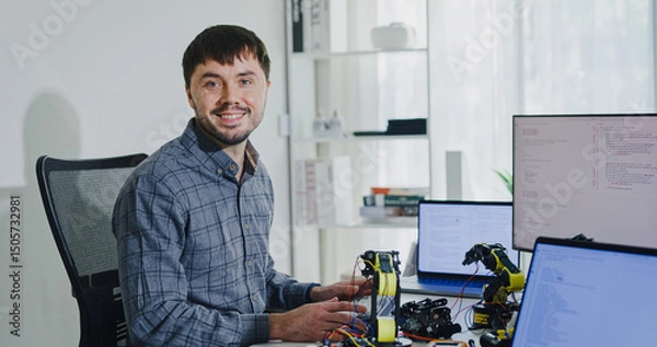 Obraz Portrait confident smiling male programmer working with robotics code AI software and looking at camera in tech office. Artificial intelligence dashboard, robotics, user interface, machine learning.