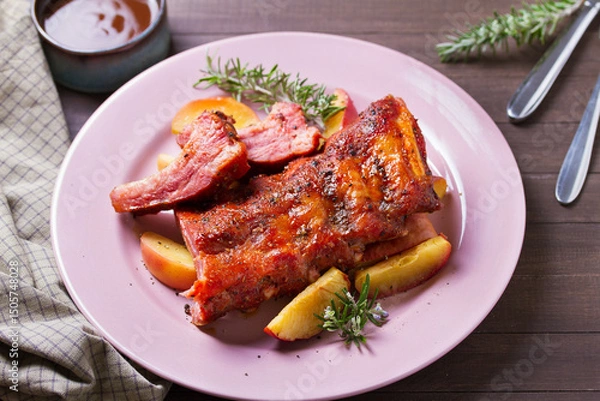 Fototapeta Roasted rack of pork ribs with apples on a plate and brown wood background