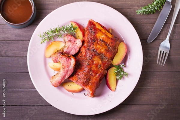 Fototapeta Roasted rack of pork ribs with apples on a plate and brown wood background. High angle view