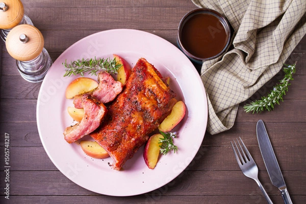 Fototapeta Roasted rack of pork ribs with apples on a plate and brown wood background. High angle view