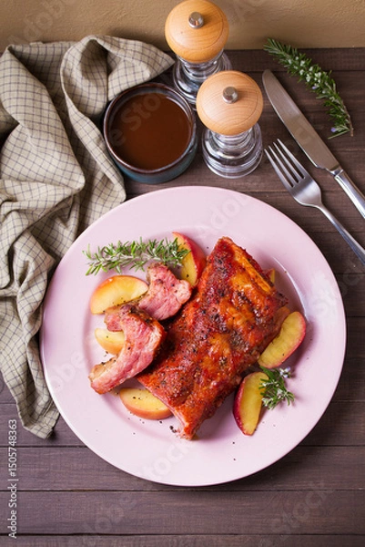 Fototapeta Roasted rack of pork ribs with apples on a plate and brown wood background. High angle view