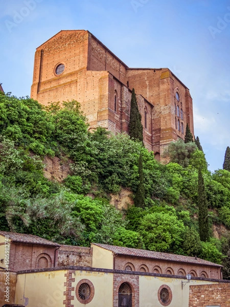 Obraz Basilica Cateriniana di San Domenico church rises above Siena, its imposing Gothic architecture framed from a low vantage point against the Tuscan sky. Travel in Italy.