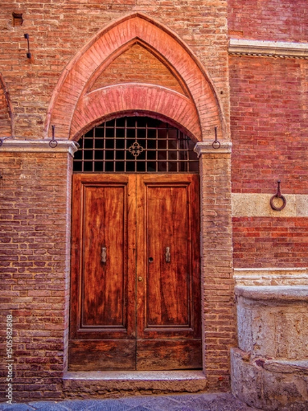 Obraz Elegant wooden door within a carved stone archway. The intricate details and textures highlight the region’s architectural charm. Travel to in Siena, Tuscany, Italy.