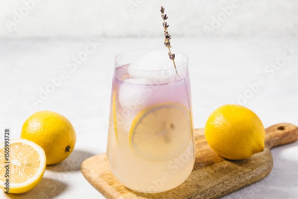 Fototapeta A refreshing lavender lemon lemonade served in a transparent glass filled with ice, garnished with a lemon slices. Summer drink and mocktail concept, natural organic lemonade recipe for holiday party.