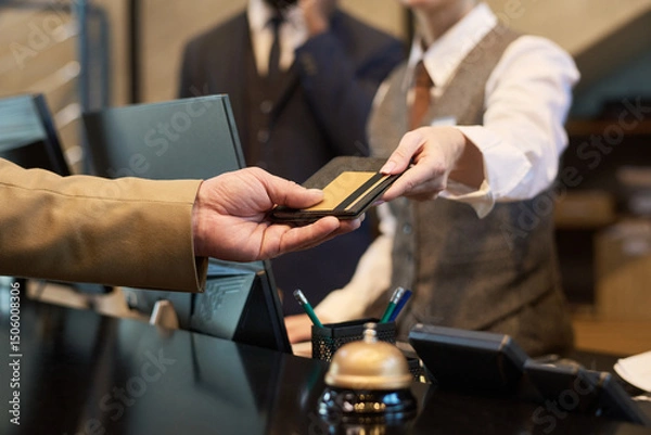 Obraz Receptionist taking credit card from guest at hotel reception for transaction processing. Elegant setup with polished service tools like bell and pen holder visible on counter