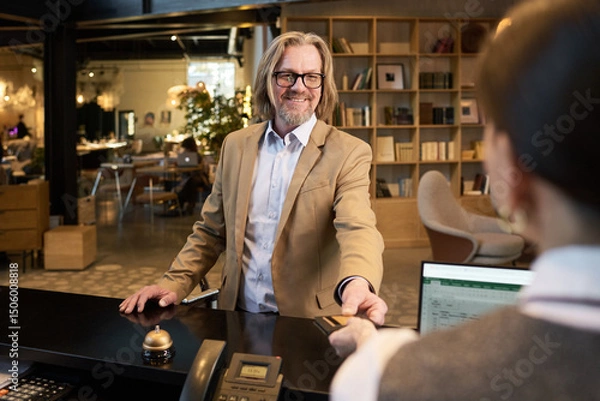 Fototapeta Elderly man with friendly smile greeting receptionist in modern, open office space with shelves and diverse seating in background