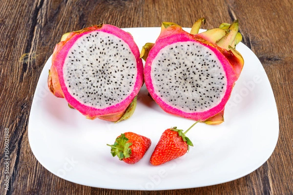 Obraz A pitahaya cut into two halves and two strawberries on a white plate.