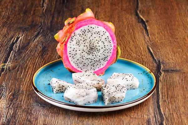 Obraz Half and sliced pieces of pitahaya pulp on a blue plate.