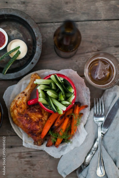 Fototapeta Top-down view of pub food: baked chicken drumsticks, rustic fries, sliced pickles, sauces, and beer. Cozy and casual atmosphere. Perfect for menus, blogs, or food delivery visuals