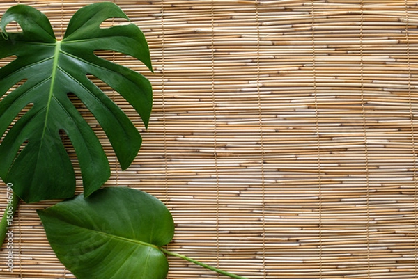 Obraz flatlay of two monstera leaves on straw reed shade surface with a space for text