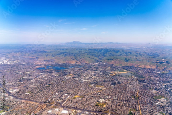 Fototapeta Aerial view of a city with rolling hills and a clear blue sky.