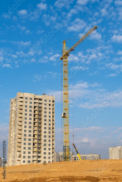 Obraz Construction of a multi-storey building with a crane against the blue sky.