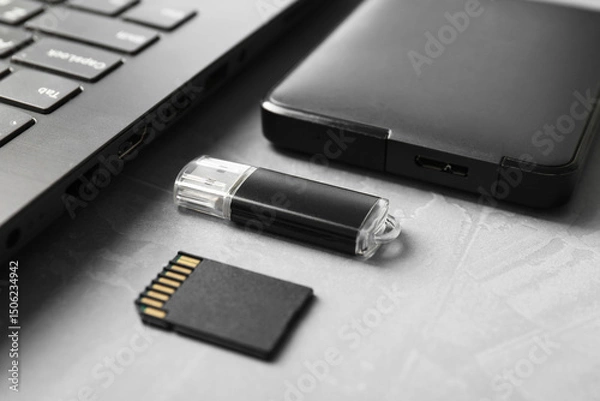 Fototapeta Flash drive, SD memory card, external hard disk and laptop on gray textured table, closeup