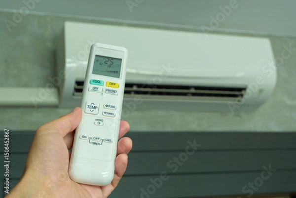 Fototapeta Man's hand using remote control open The air conditioner is cooled to 25 degrees Celsius in his bedroom. Health concepts and energy savings